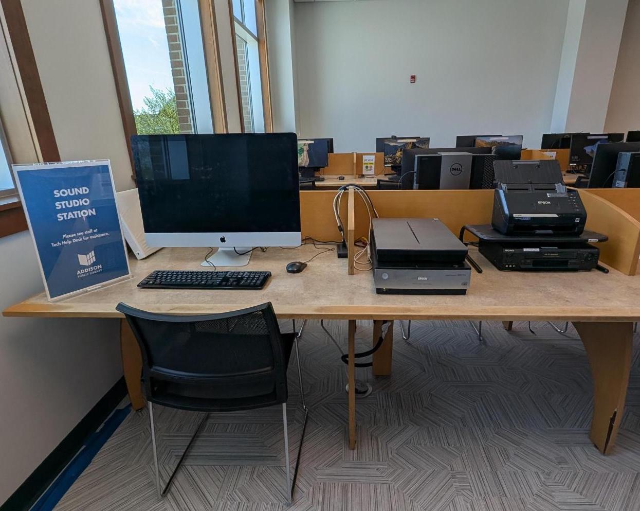 Photo of the Sound Studio Station located in the temporary computer lab on the 2nd floor. Shows an iMac with a flat bed scanner, photo batch scanner, and VHS player.