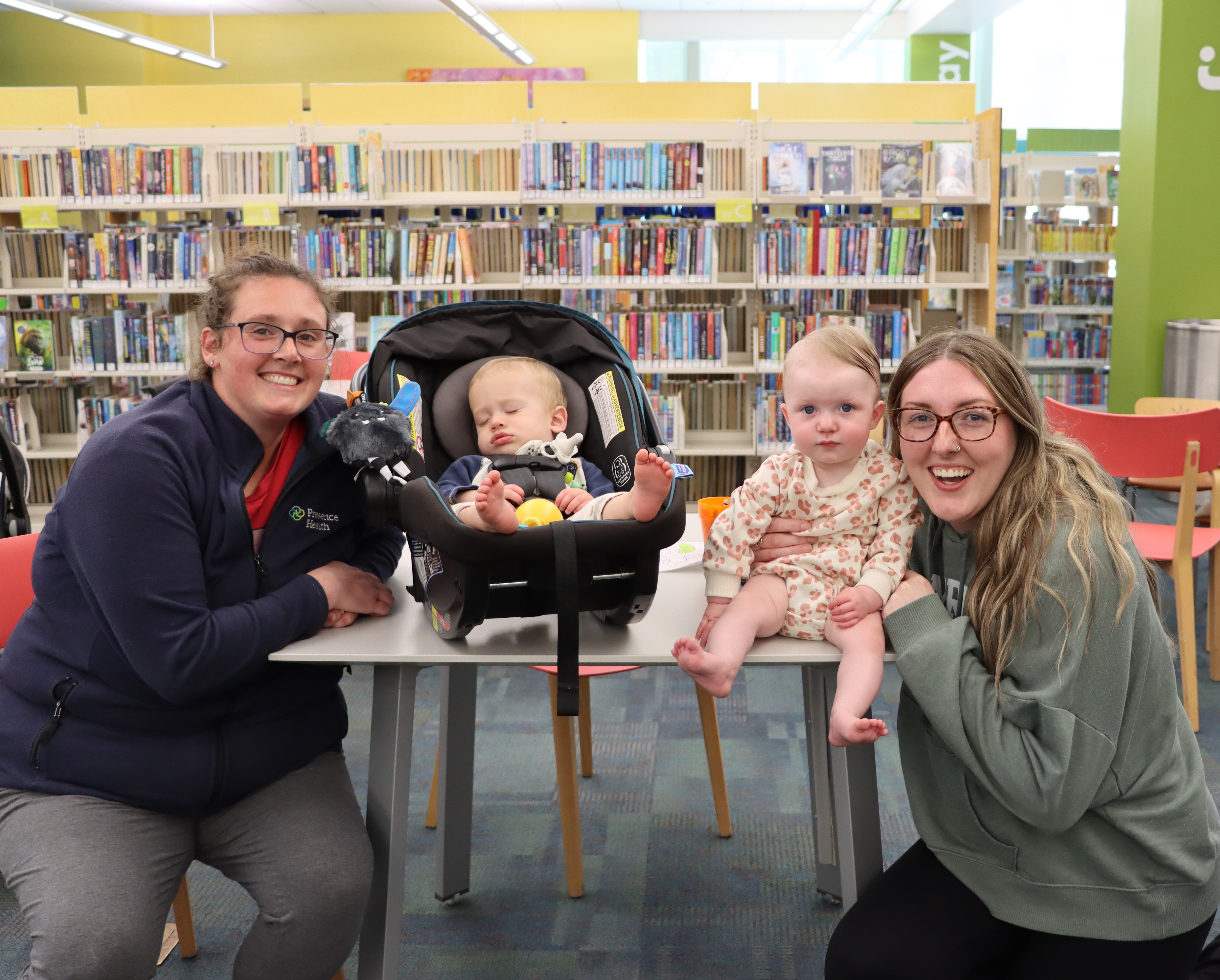 two women smiling and posing at a table with their young children