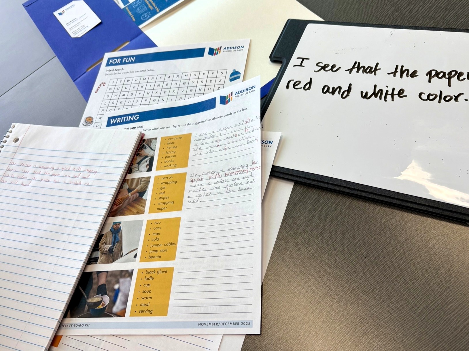a spiral notebook, various worksheets, and a personal dry erase board lie on a tabletop