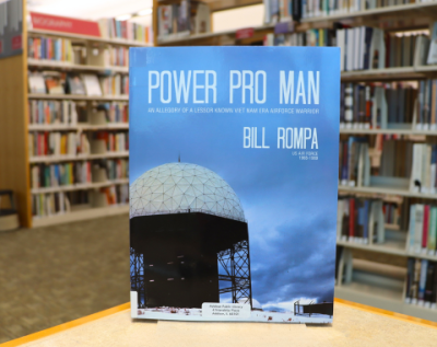 photo of the book Power Pro Man by Bill Rompa on display on a table, with library shelves in the background