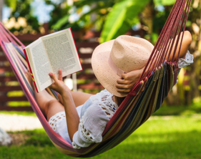 person with a sunhat lounging in a hammock reading a book on a sunny spring day