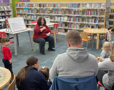 librarian sitting in front of small children and families and performing a storytime