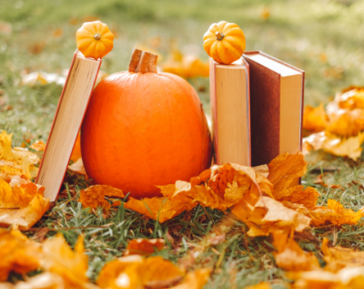 a mini pumpkin surrounded by books propped up against it, sitting on a pile of fall leaves