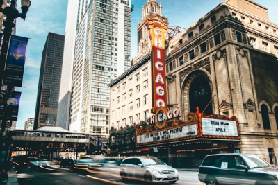A street in Chicago with cars passing by in front of a building with a vertical red sign that says "Chicago"