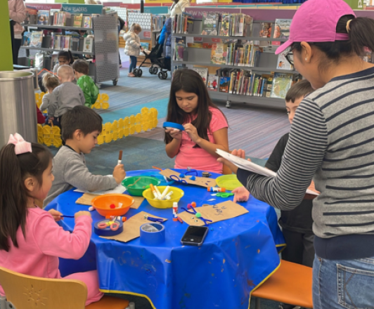 a group of children and an adult participating in a craft at a table