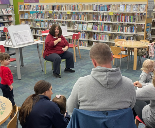 librarian sitting in front of small children and families and performing a storytime