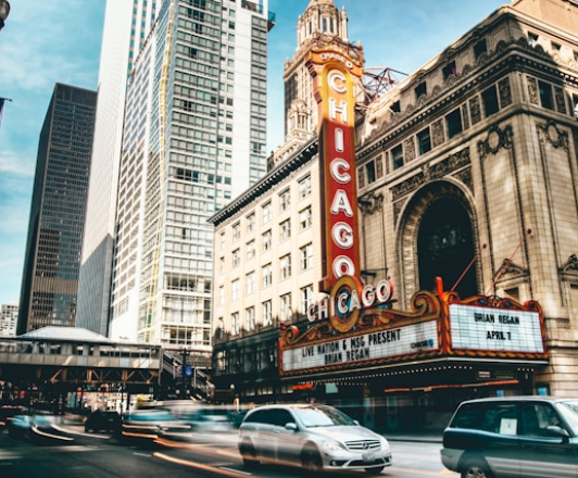 A street in Chicago with cars passing by in front of a building with a vertical red sign that says "Chicago"