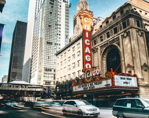A street in Chicago with cars passing by in front of a building with a vertical red sign that says "Chicago"